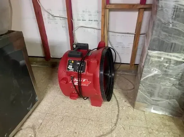 A red air mover beside an opened lower wall with plastic sheeting, representing drying work in Cerritos.
