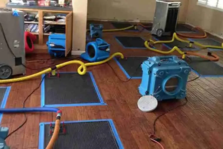Floor drying mats, air movers and a dehumidifier set up on hardwood flooring