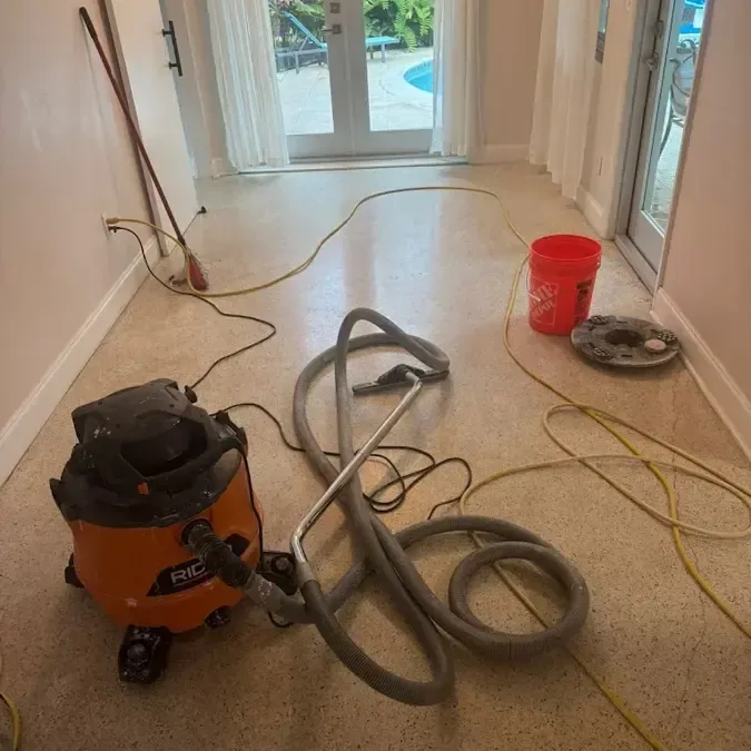 Wet vacuum, hoses and a bucket set up on a terrazzo floor to pull up standing water